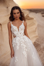 The Zafira bridal gown with a flowing tulle skirt and floral lace accents, styled with a groom in a beige suit, embodies timeless romance.