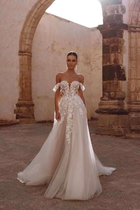 The Ariella wedding gown by DAMA Couture features a corset with exposed boning and rich floral lace appliqués, creating an ethereal elegance.