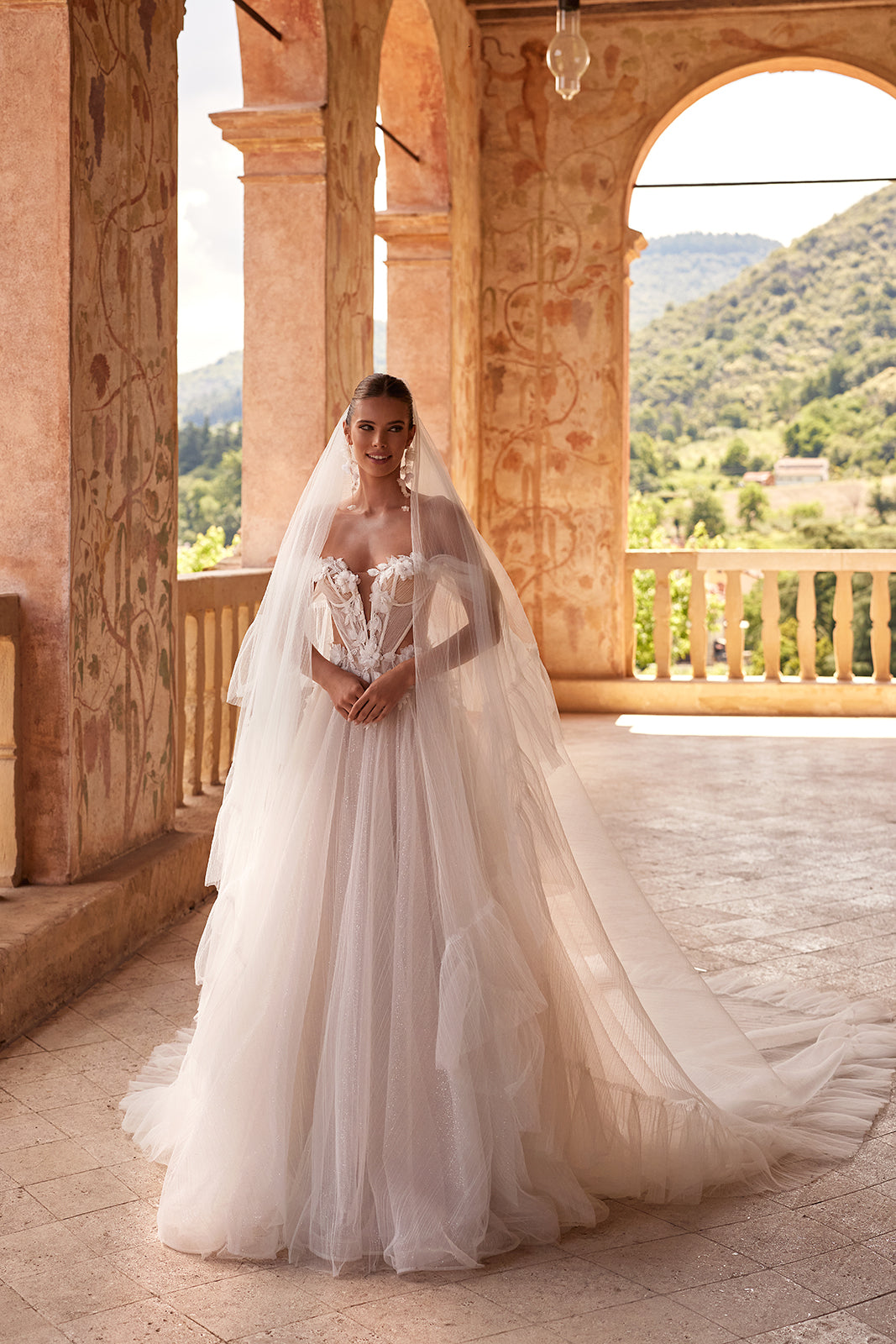 Full-length view of Avalon wedding dress with a long veil beneath an arcade