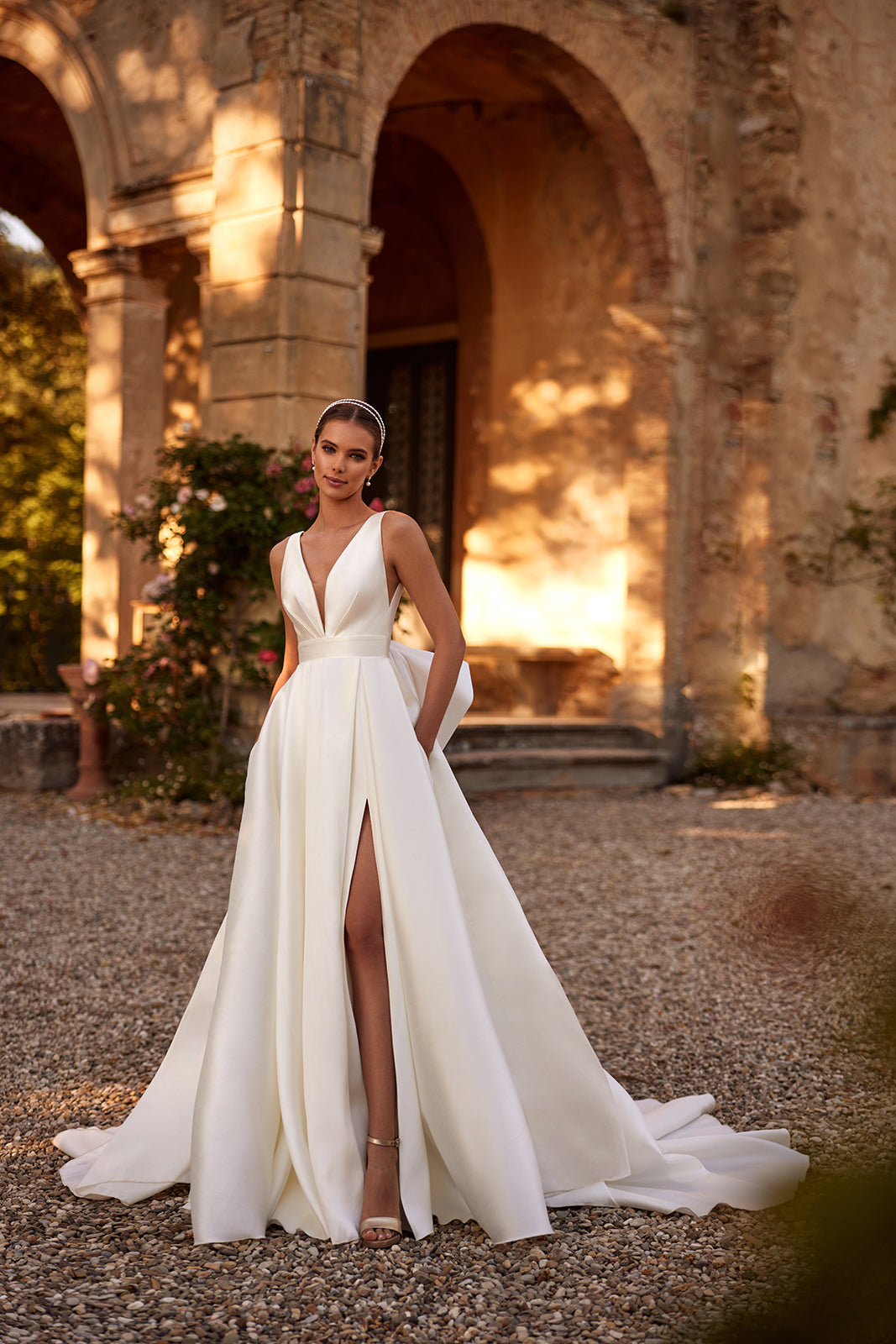 Full-length Margo wedding dress by a villa's arcade, with a thigh-high slit