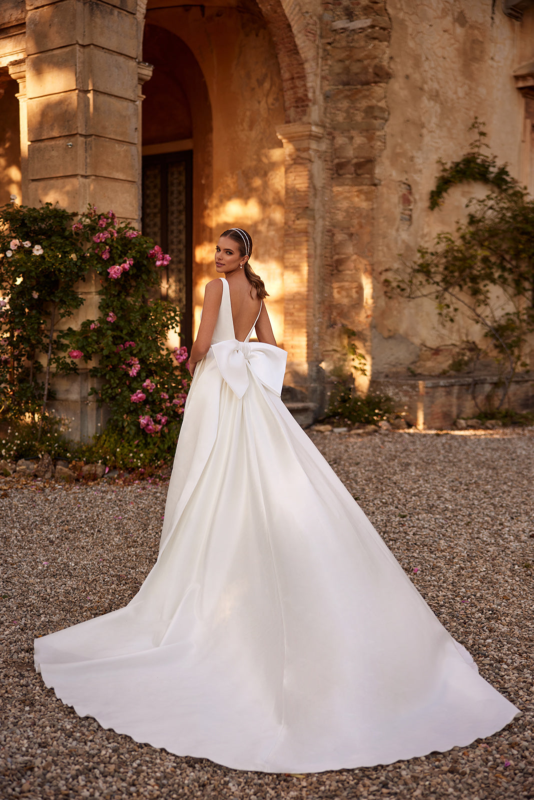 Margo wedding dress from behind, with an open back and satin train resting on gravel