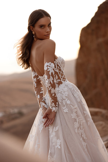 The Nabila bridal gown with an off-the-shoulder design and dramatic tulle skirt embodies classic romance and modern sophistication.