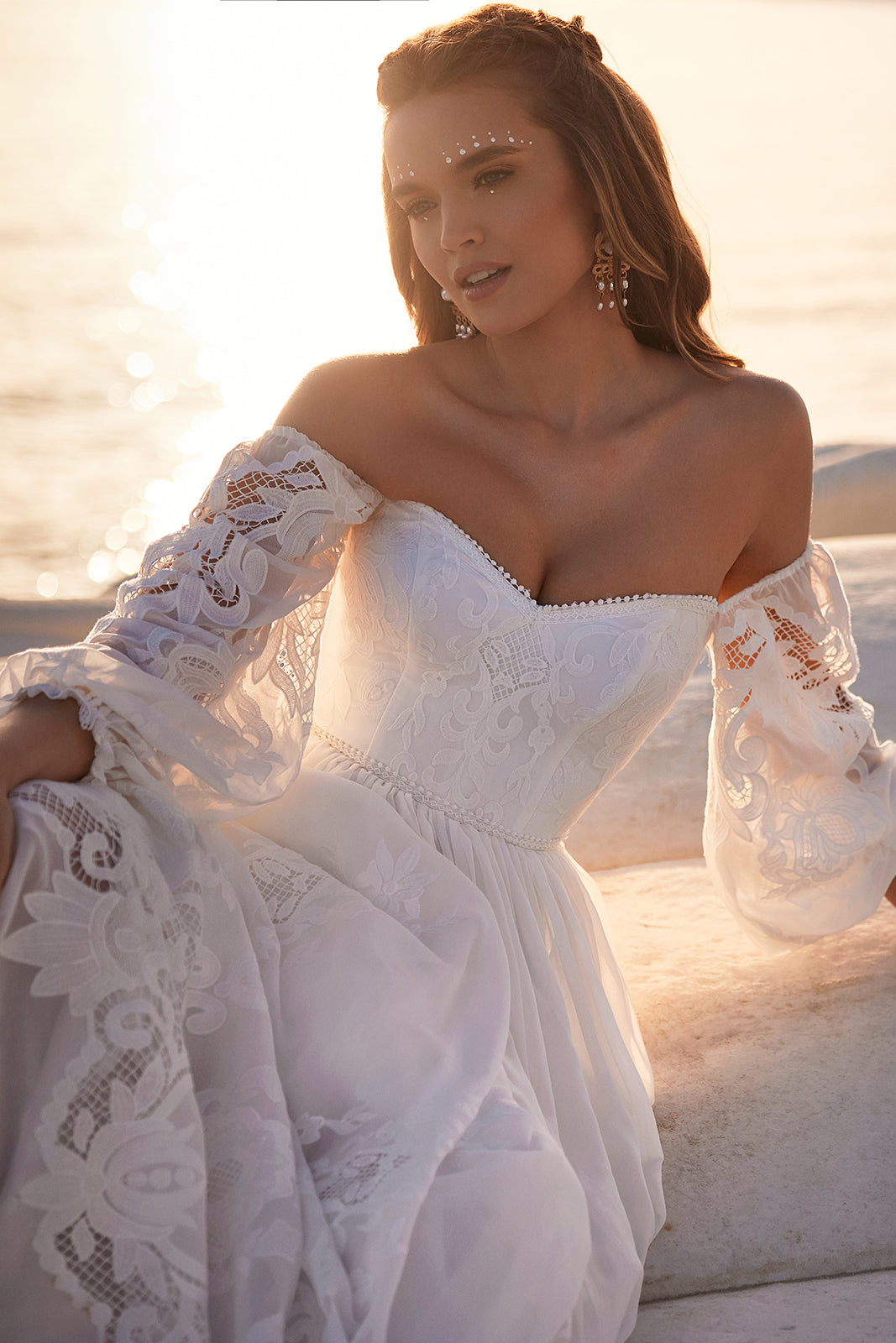Seated view of Rania with an off-the-shoulder neckline and openwork lace sleeve