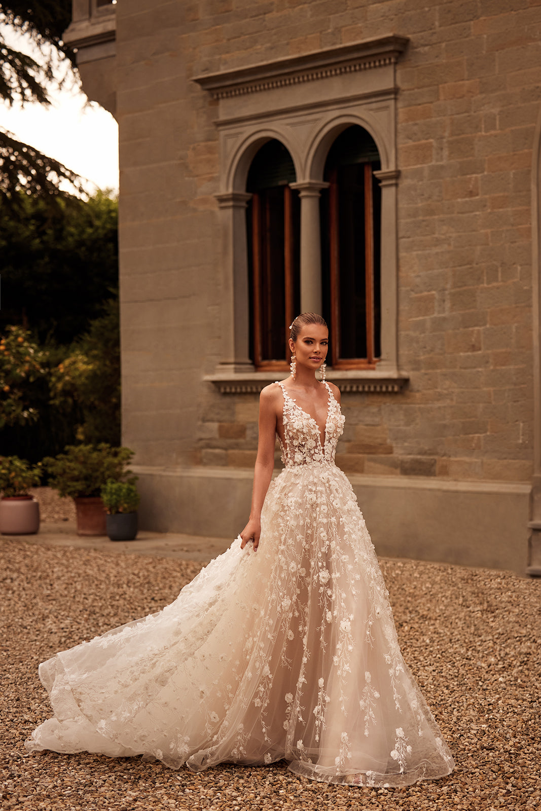 Samsara at full length outside a villa, with floral lace on tulle and a spread train