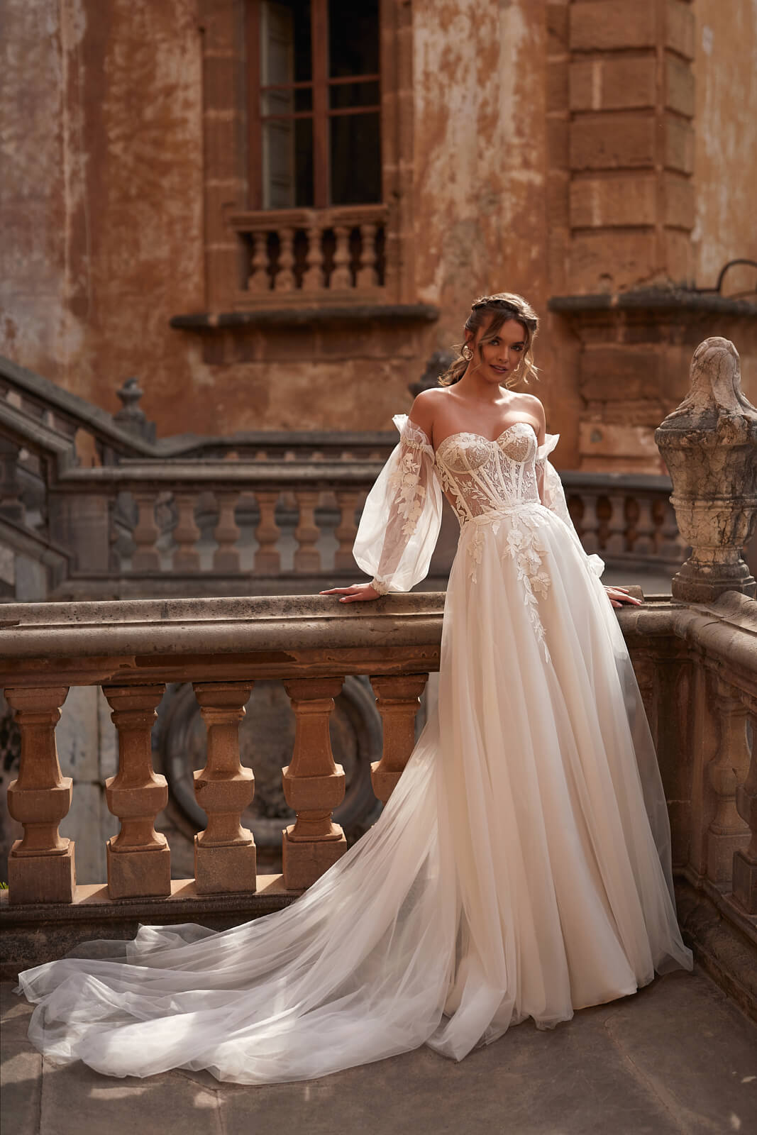 Full-length Hermiona A-line wedding dress beside a stone balustrade, with a tulle train
