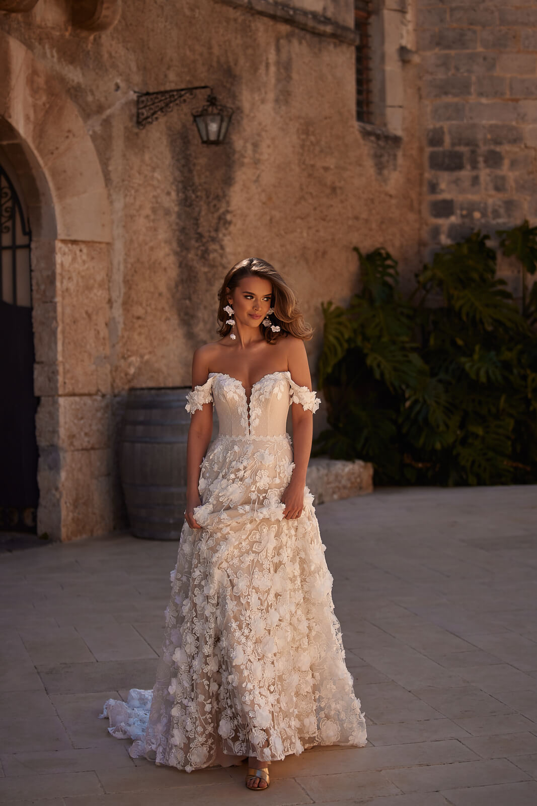 Front view of Olivia in a courtyard, bare shoulders above floral appliqués on the skirt