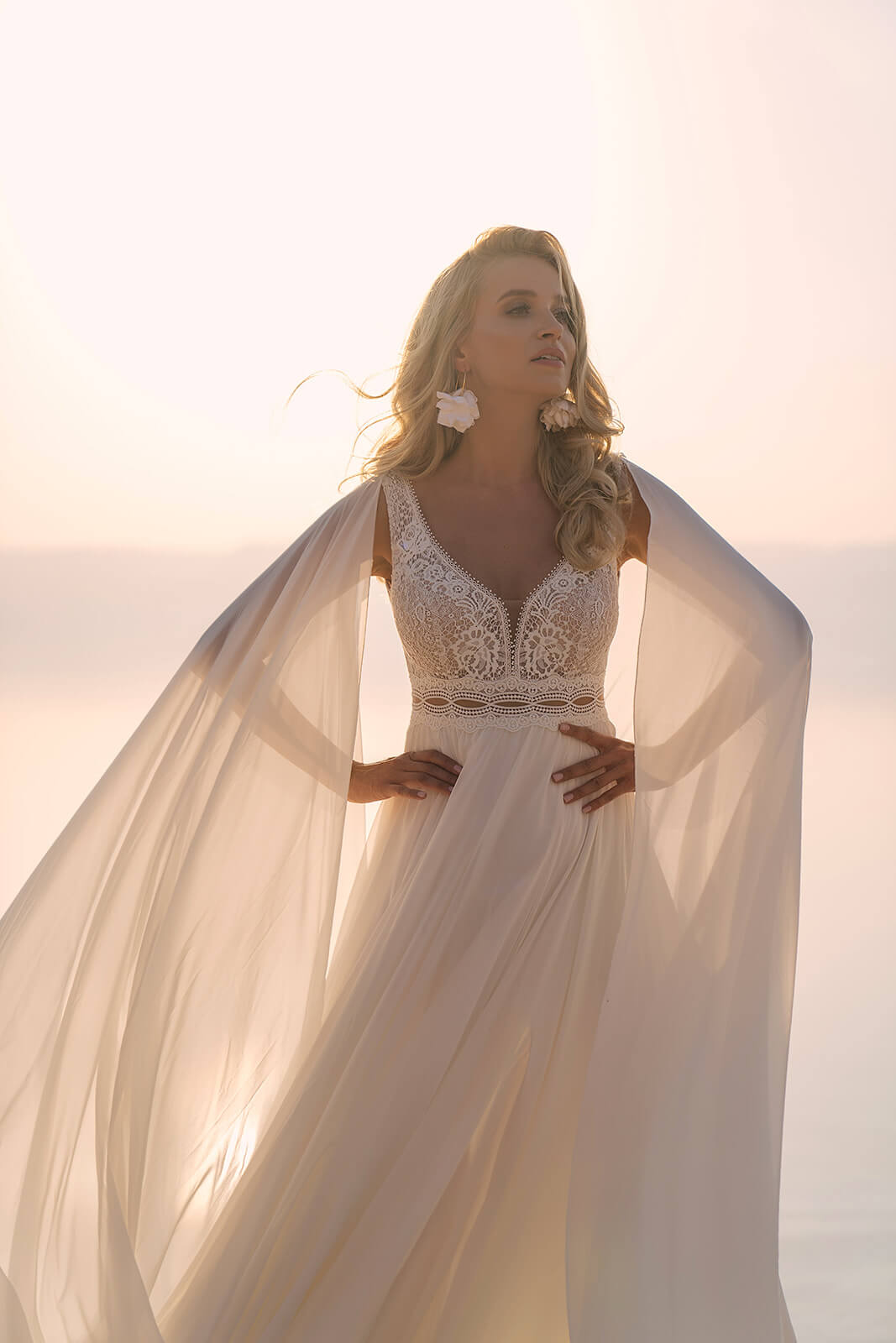Backlit half-length view of Atena wedding dress, with a lace bodice and flowing chiffon