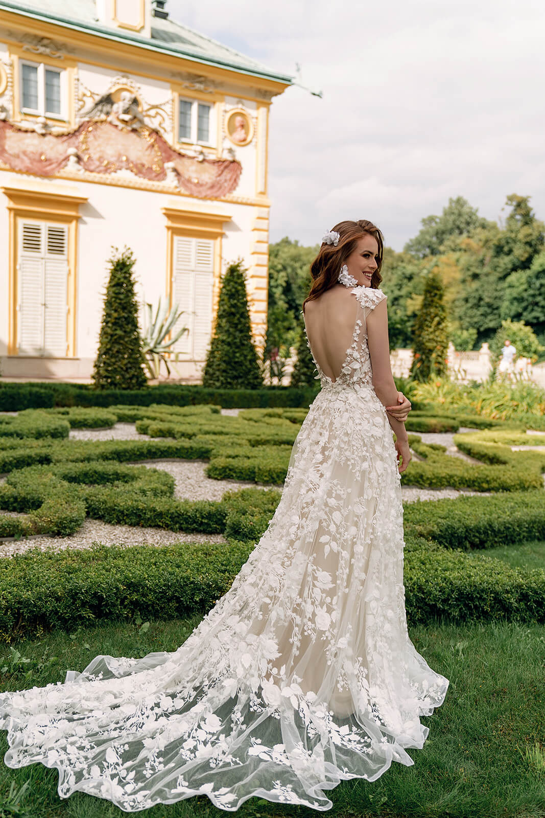 Azalea wedding dress from behind in a palace garden, with its lace train resting on the lawn