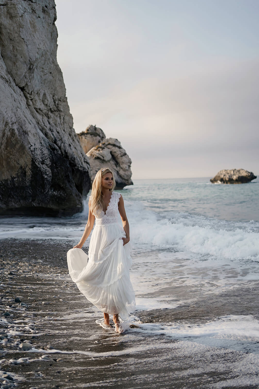 Back view of Lidia wedding dress stepping into shallow water, the skirt gathered up