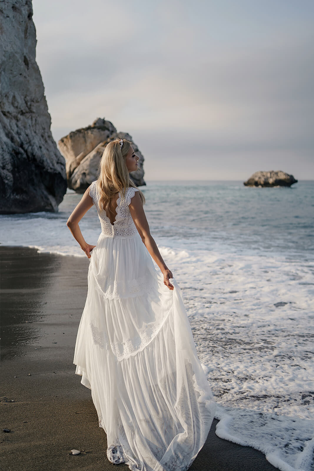 Lidia wedding dress from behind on the beach, its light skirt lifted and held to one side