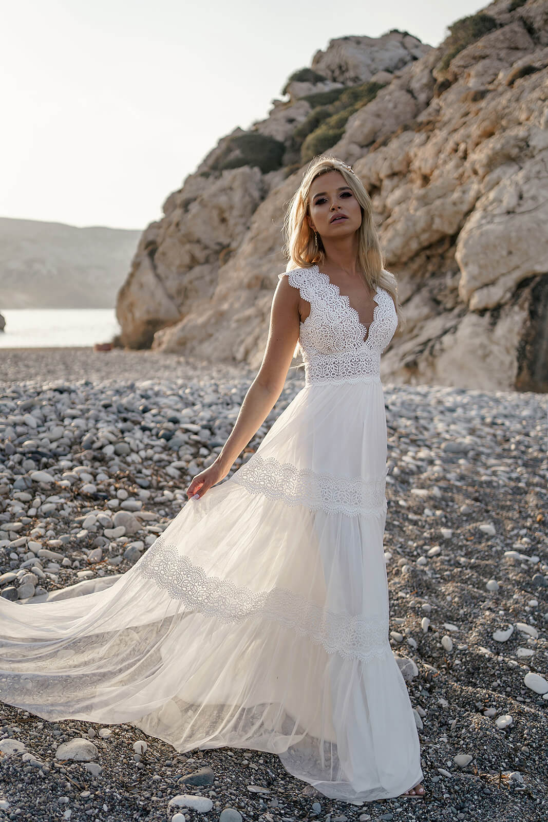 Full-length front view of Lidia wedding dress against seaside rocks, with its light tulle skirt