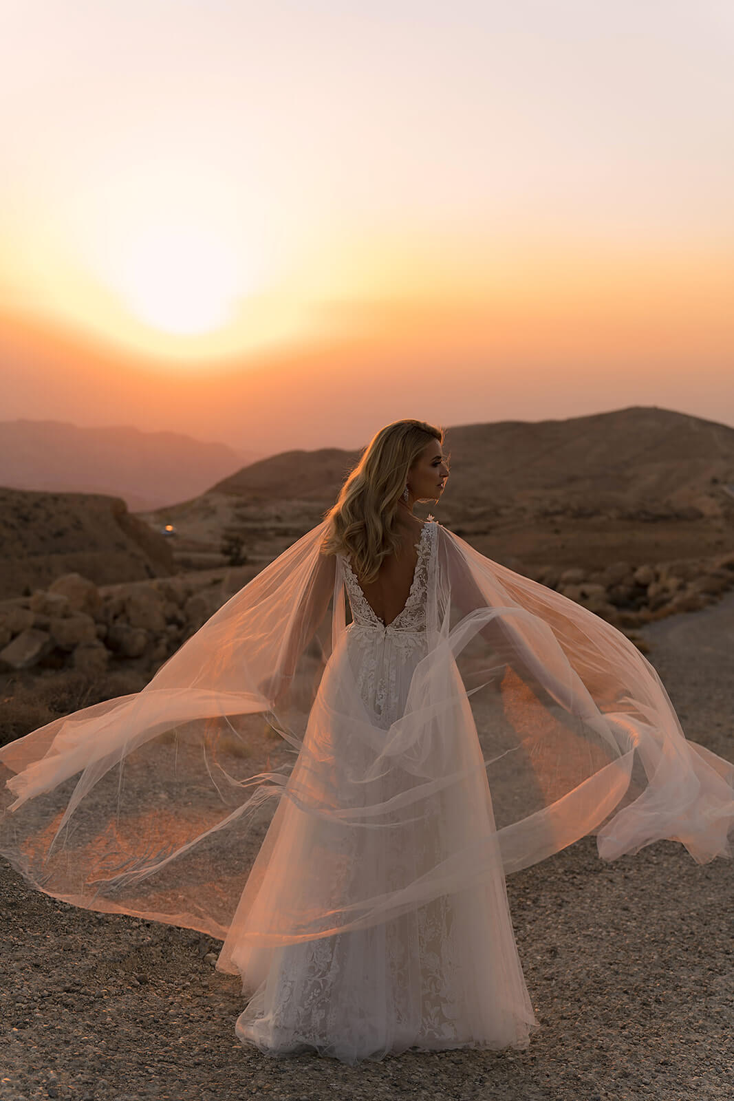 Back view of Linda wedding dress above the desert, with its wide tulle cape blowing in the wind