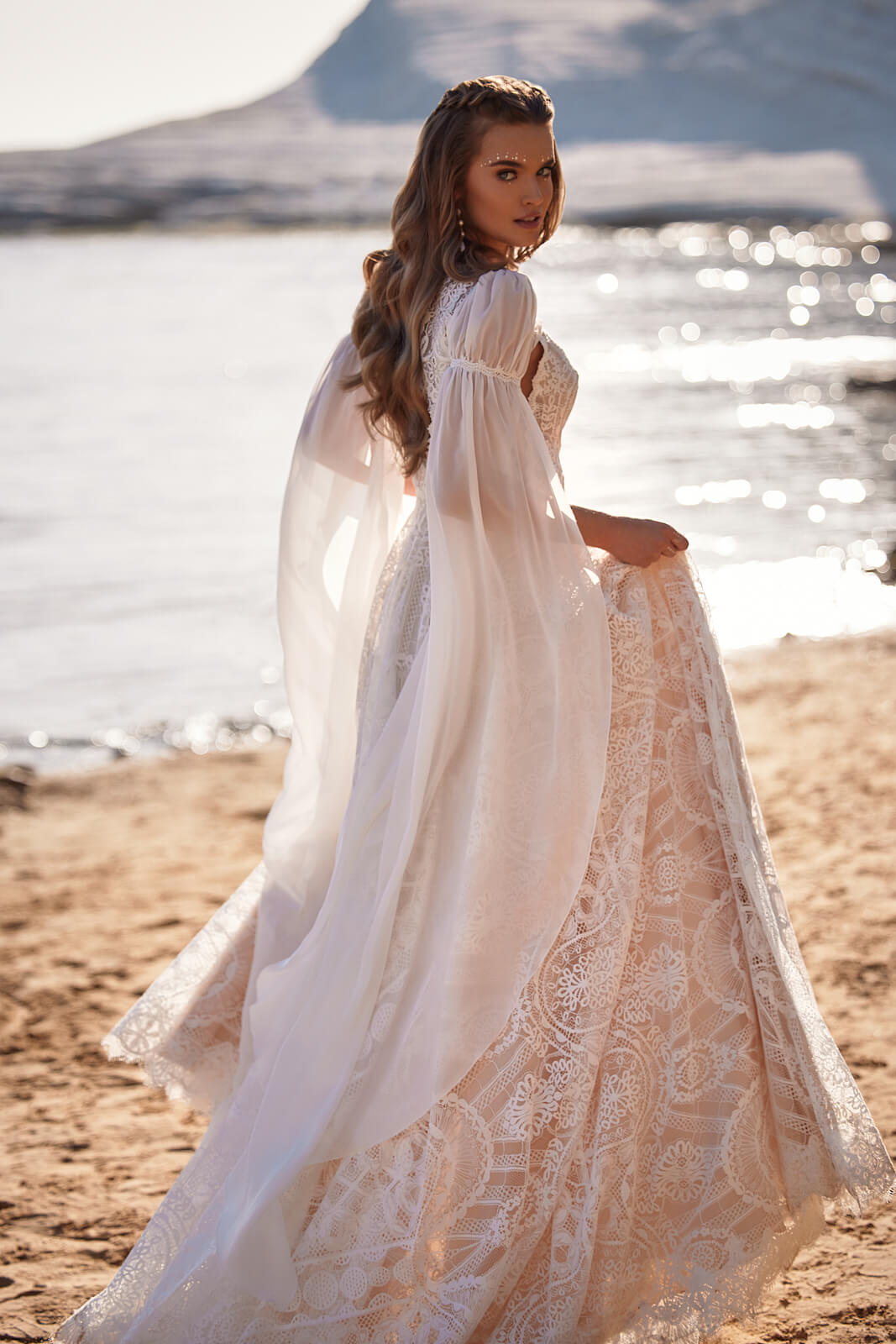 Hope wedding dress from behind on the beach, the bride lifting its A-line skirt in one hand