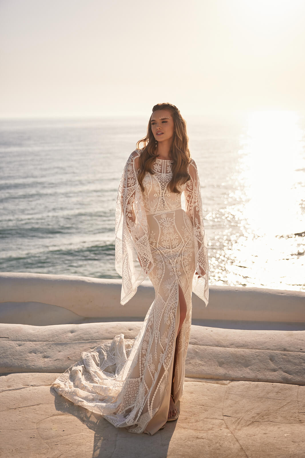 Persefona at full length from the front, sleeves spread wide and skirt slit visible