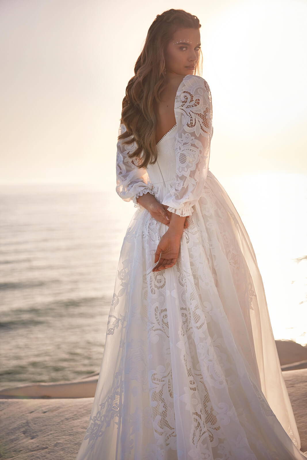 Over-the-shoulder view of Rania beside the sea, with openwork lace on puff sleeves