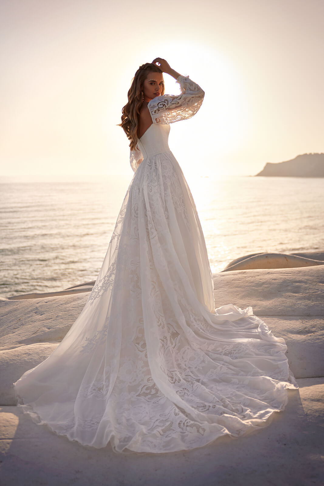 Rania from behind, its broad lace train spread across a rock