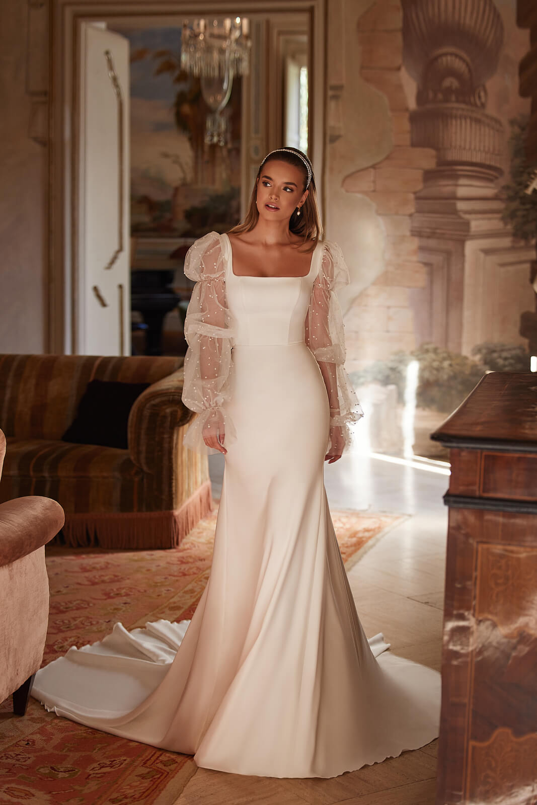 Clara wedding dress indoors, with a narrow satin silhouette, square neckline and train