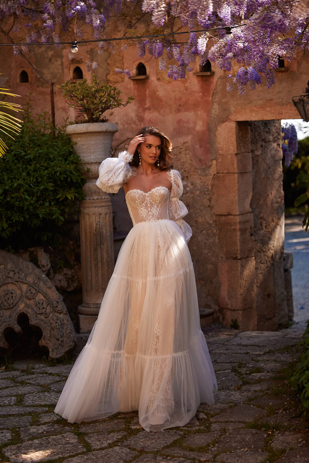 Full-length Loretta wedding dress in a courtyard beneath flowering wisteria, with a layered tulle skirt