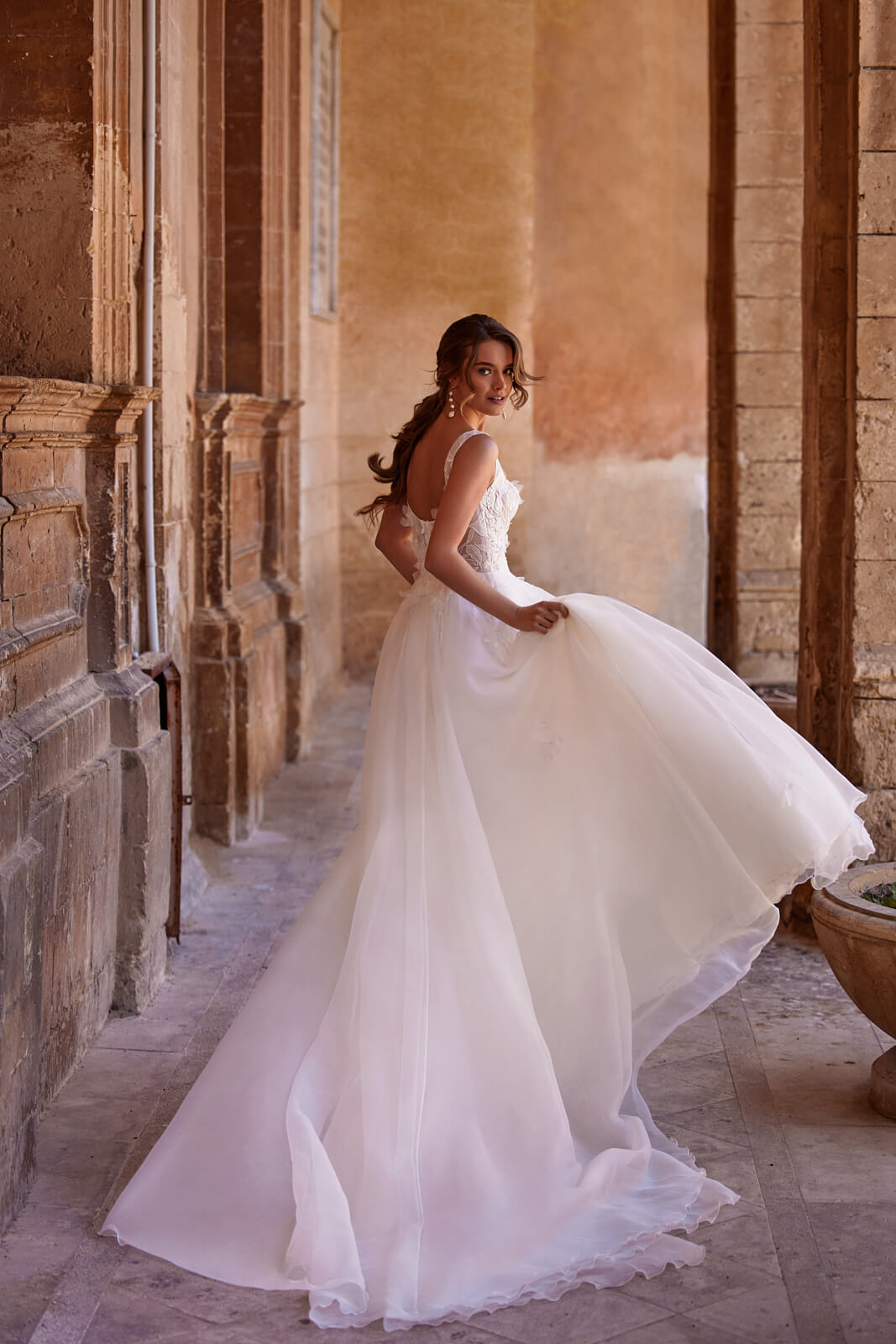 Lucy wedding dress from behind in motion beneath an arcade, with a wide layered organza skirt