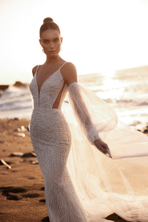 Beaded wedding dress with plunging V-neckline, pearl detailing, and sheer puff sleeves for a modern bridal look.