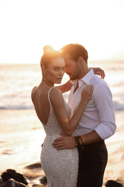 Pearl-embellished lace bridal gown with a low back, photographed in a romantic seaside sunset.