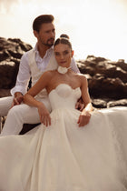 The Cholly bridal gown with a corset top and voluminous skirt, beautifully photographed among coastal rocks.