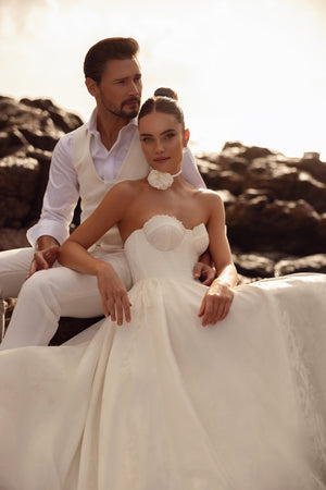 The Cholly bridal gown with a corset top and voluminous skirt, beautifully photographed among coastal rocks.