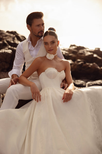 The Cholly bridal gown with a corset top and voluminous skirt, beautifully photographed among coastal rocks.