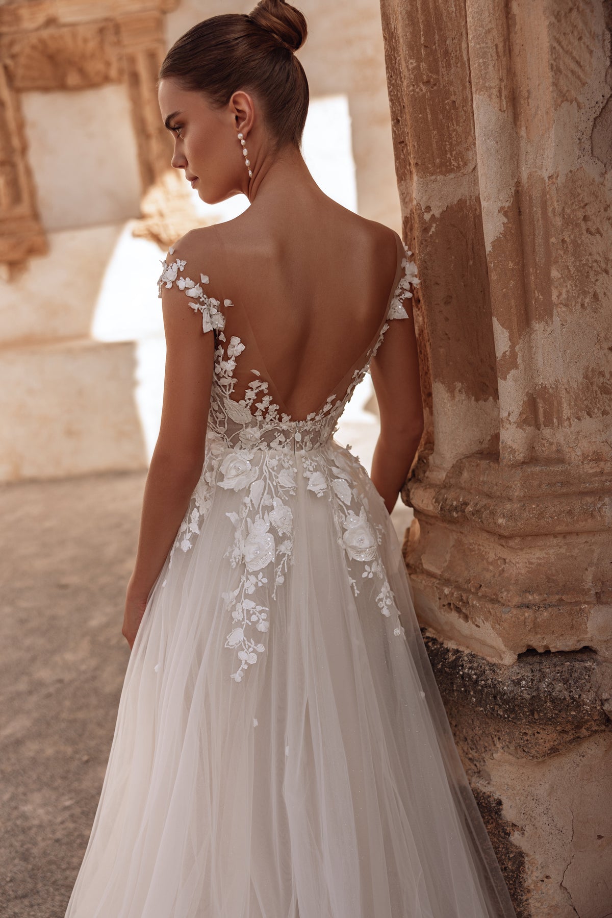 The Andrea wedding dress with an open back and long flowing train embodies ethereal elegance and modern romance.