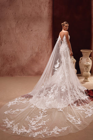 The Aspasia bridal dress features a long lace train and floral-detailed cape for an ethereal, romantic finish.