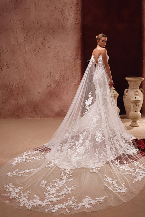 The Aspasia bridal dress features a long lace train and floral-detailed cape for an ethereal, romantic finish.