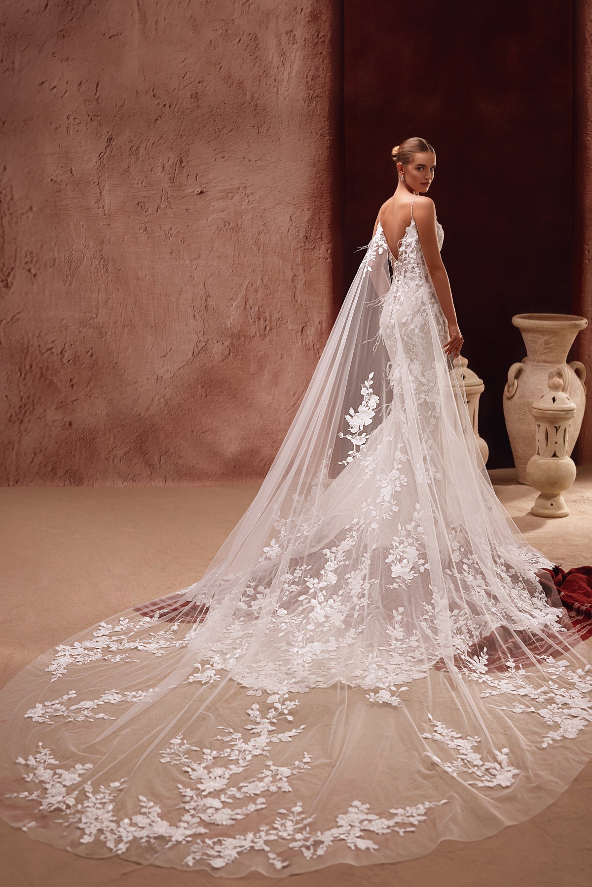 The Aspasia wedding gown with a dramatic lace train and floral-embroidered cape creates an unforgettable bridal silhouette.