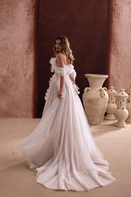 The Bella bridal gown features off-shoulder draping and a long airy train for a graceful, fairytale look.