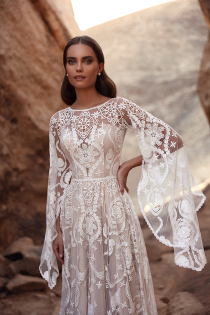 The Dune bridal gown with a long lace train and bell sleeves evokes ethereal elegance and desert romance.
