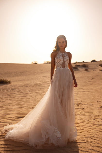 The Ellie bridal gown showcases a sheer halter neckline and soft tulle skirt with floral detailing, perfect for an ethereal bride.