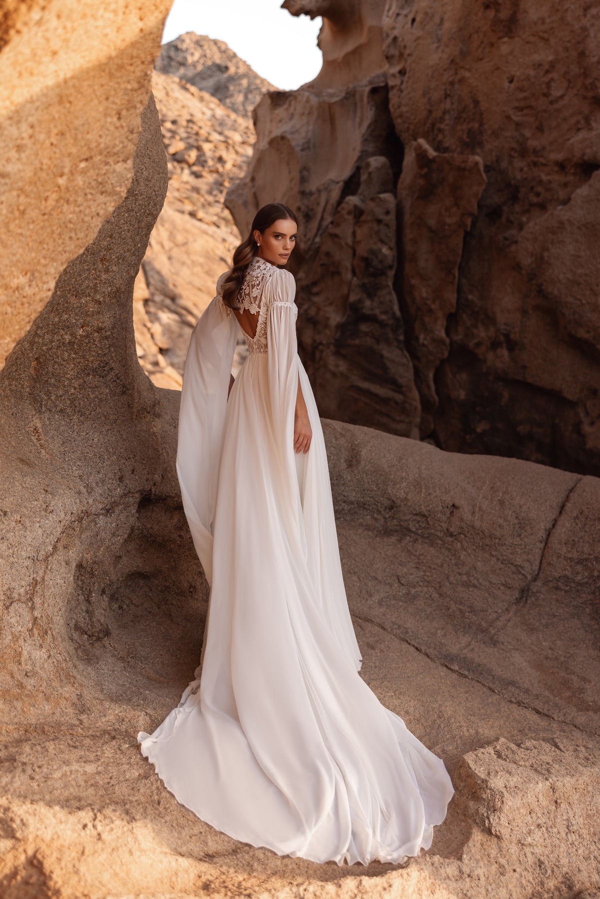 Full-length back view of Etra wedding dress, its open chiffon sleeves falling like a cape