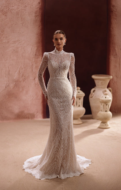 The Henriette bridal gown showcases intricate lace, long sleeves, and a high neckline adorned with pearls for a refined, royal-inspired look.