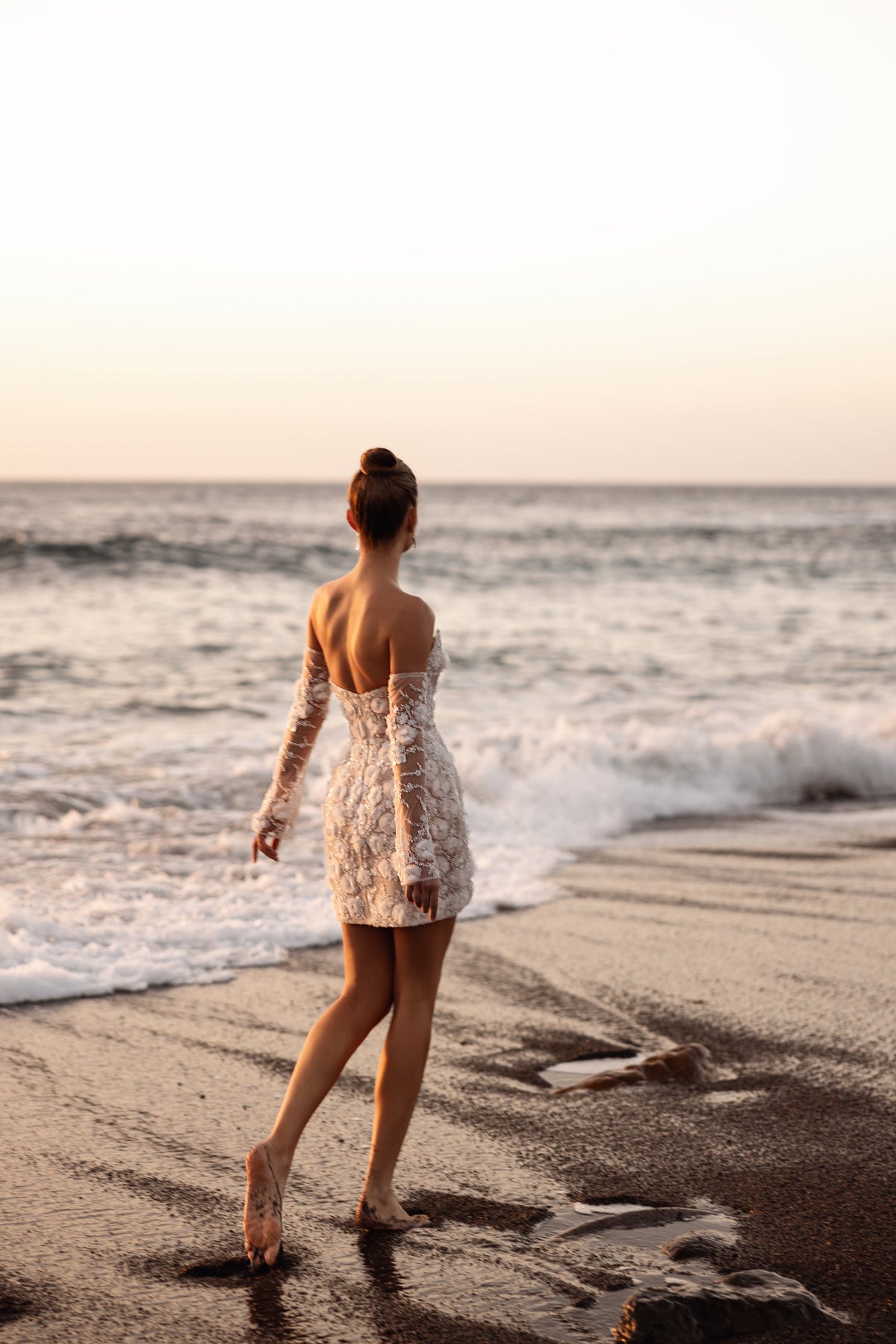 Full-length back view of Kayla short wedding dress beside the water at sunset