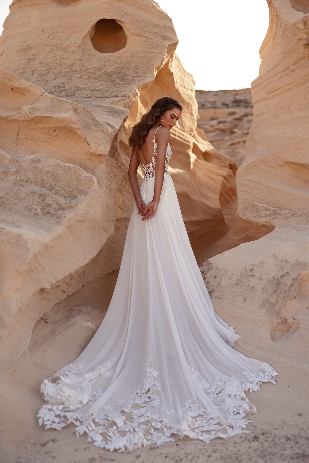 Back view of Malika wedding dress, with the floral lace-edged train spread across the sand