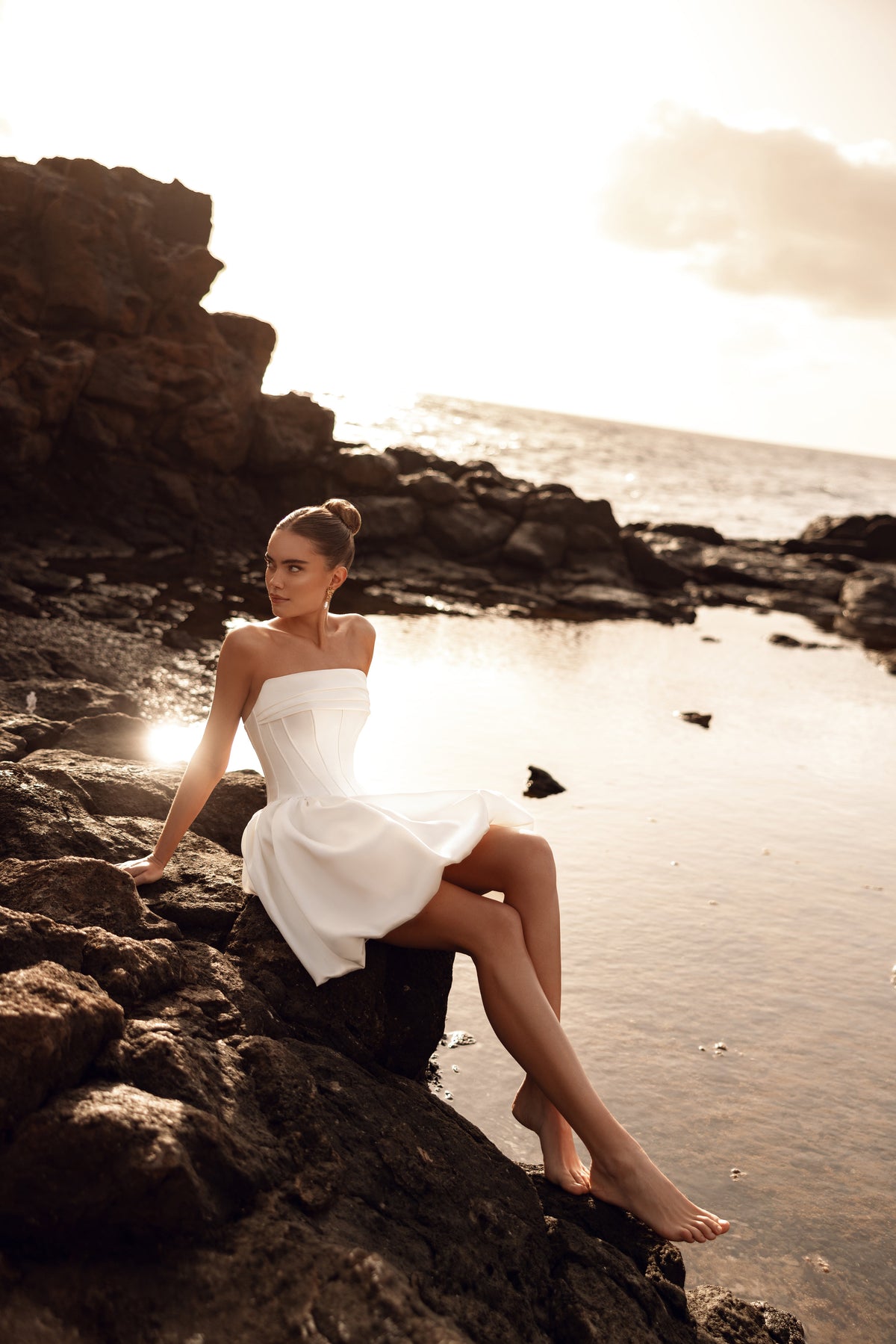 Side view of a bride seated on rocks in Martini mini wedding dress