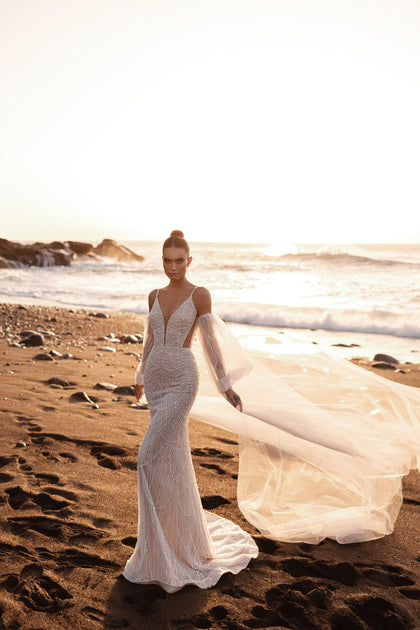 Slim mermaid bridal gown with plunging V-neck and long sweeping veil, perfect for seaside weddings.