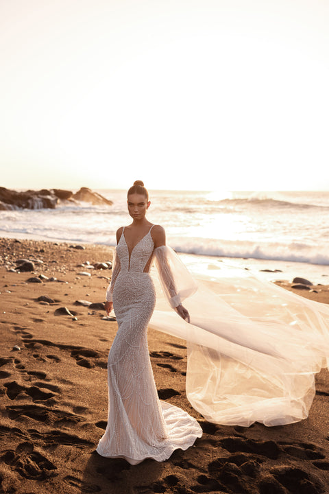 Fitted mermaid wedding dress with a deep V-neckline and flowing chapel-length veil on the beach.