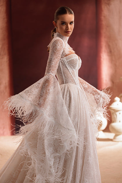 The Michelle bridal dress with flared lace sleeves and feather details exudes confidence and modern sophistication.
