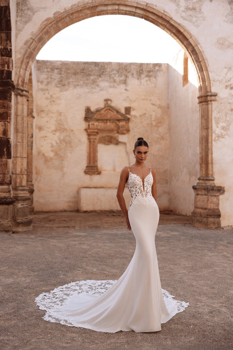 The Munira bridal gown showcases a plunging V-neck lace bodice with detailed embroidery and a refined mermaid-style fit.