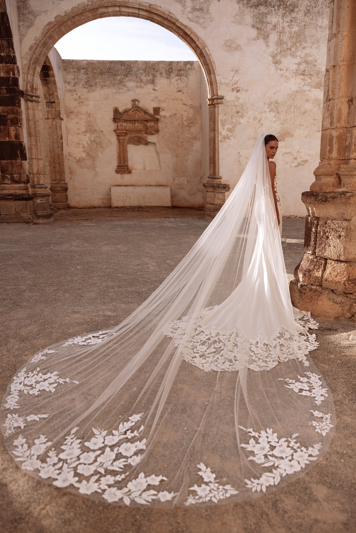 Munira cathedral wedding veil with floral lace appliqués, creating a dramatic bridal look in historic ruins.