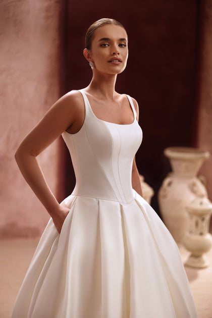 The Nicolette wedding dress features a clean satin bodice with straps and a voluminous princess skirt for a timeless bridal look.