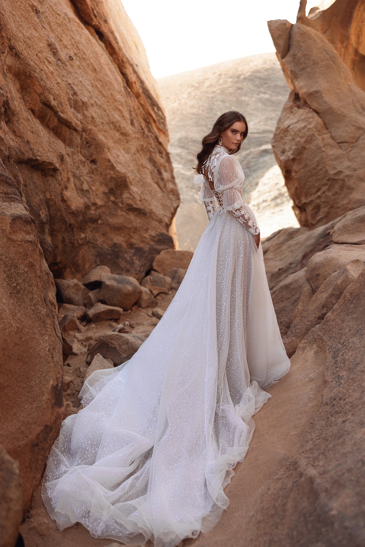 Back view of Oasis wedding dress, its sparkling tulle train falling over desert rocks