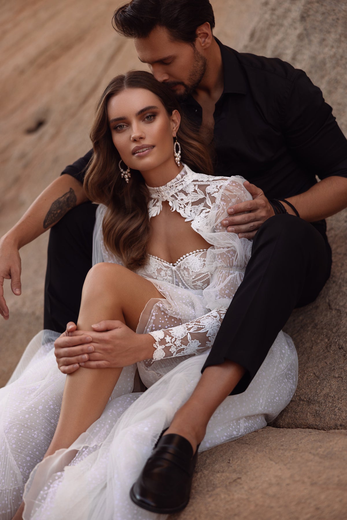 Seated bride in Oasis wedding dress on a rock, with puff sleeves and a sweetheart neckline