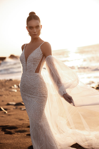 The Rebecca mermaid wedding dress with spaghetti straps and pearl beadwork glows under the sunset, creating a timeless beach bridal look.