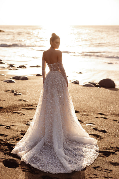 The Reem wedding dress with an illusion corset and 3D floral embellishments highlights feminine elegance under the sunset glow.